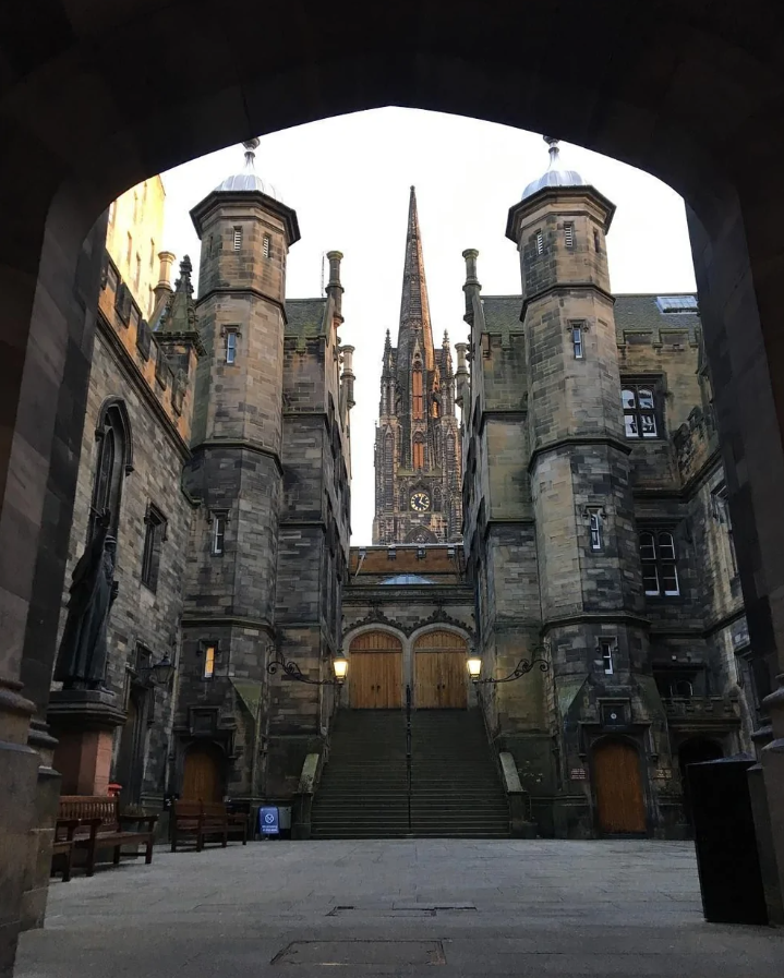 Historická gotická architektúra s vežou a širokými schodiskami v kamennom dvore osvetlenom lampami.