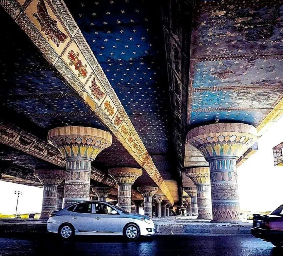 Farebné zdobené stĺpy pod mostom v štýle starovekého Egypta s autami prechádzajúcimi pod nimi.