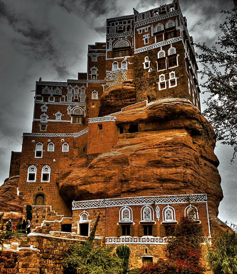 Historická budova na skalnom útese s unikátnou architektúrou pod zamračenou oblohou.
