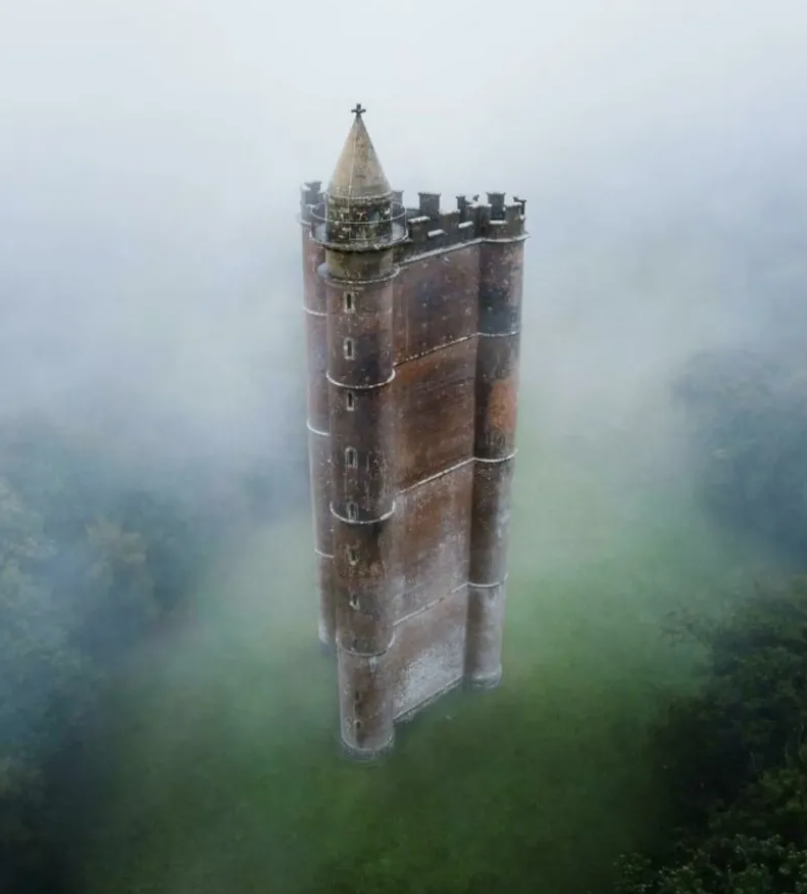 Starodávna tehlová veža obklopená hmlou, stojaca osamotene v zeleni.
