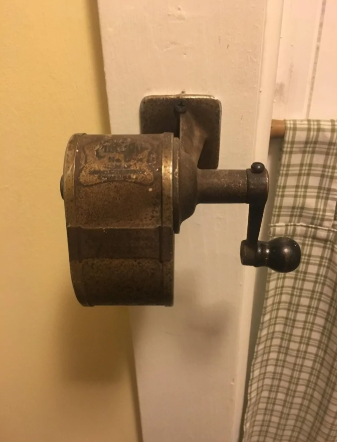 Staromódny nástenný mlynček na kávu s kľukou na bielej stene.