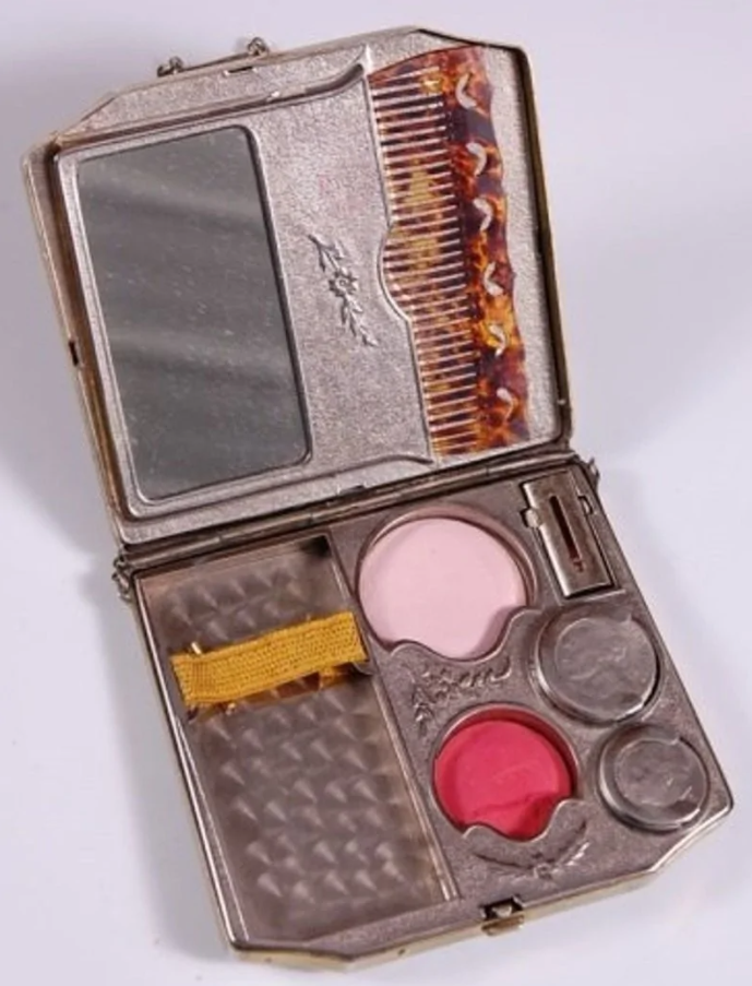 Otvorená vintage dámska pudrenka s rúžom, zrkadlom a hrebeňom; kompaktné riešenie pre krásu na cestách.