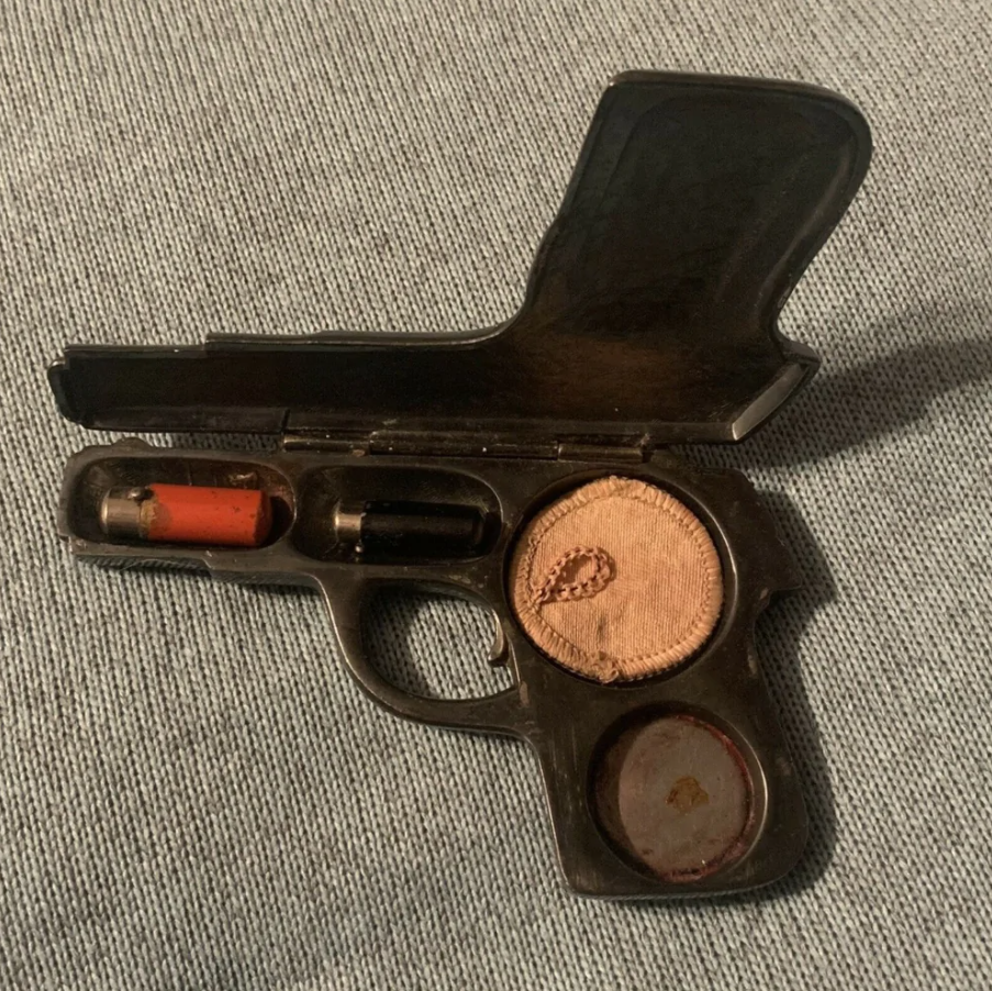 Očná tieňová paletka v tvare revolvera, otvorená na šedom pozadí.