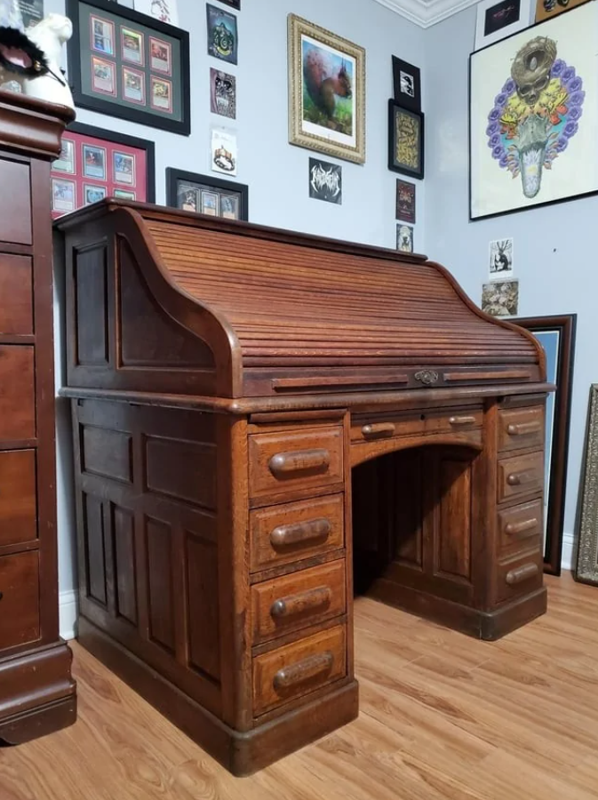 Starý drevený písací stôl s roletkou v miestnosti s obrazmi na stenách.