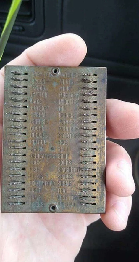 Kovová doštička s vygravírovaným zoznamom základných potravín držiacu v ruke pre nákupné účely.