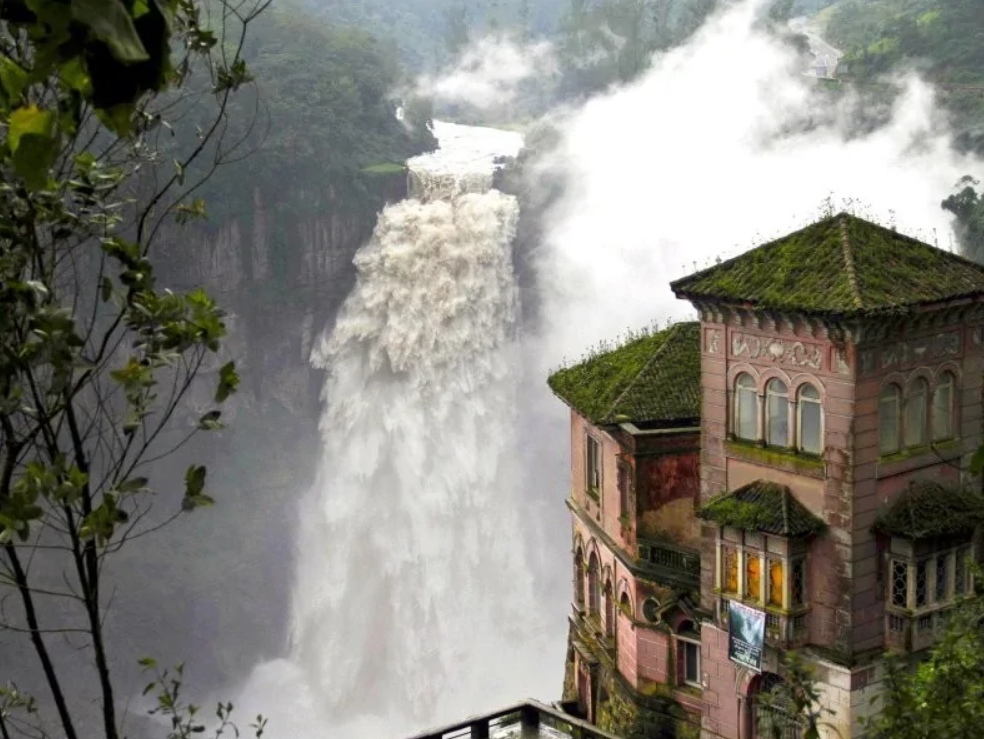 Vodopád v džungli vedľa starobylej budovy obklopenej hustou zelenou vegetáciou a hmlou.
