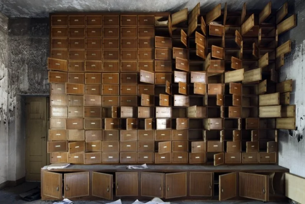 Stena s otvorenými zásuvkami v starej miestnosti, ktoré pôsobia chaoticky a zanedbane, odhaľujúce prach a neporiadok.