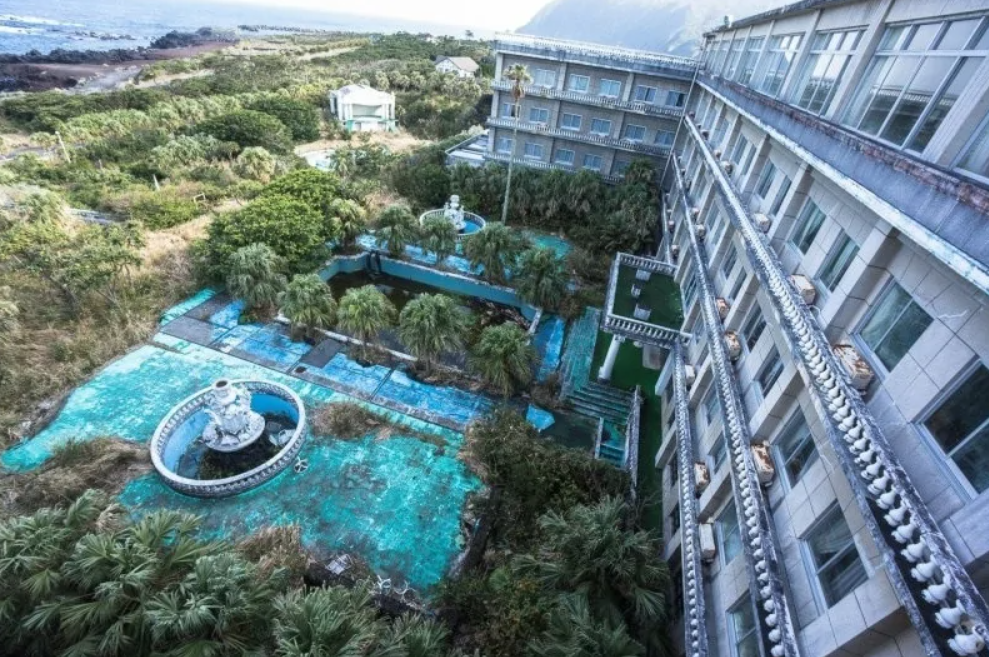 Opustený hotel s fontánou a zarastenou záhradou pri pobreží.