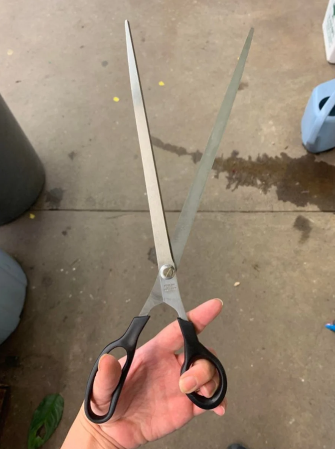 Veľké nožnice s čiernou rúčkou držiace v ruke na betónovej podlahe.