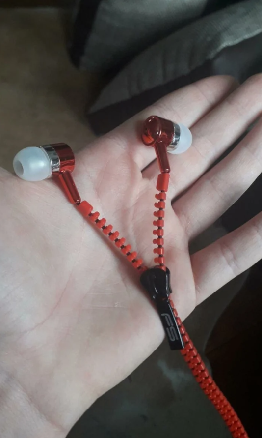 Červené slúchadlá v tvare zipsu ležia na dlani, moderný dizajn a praktické usporiadanie káblov.