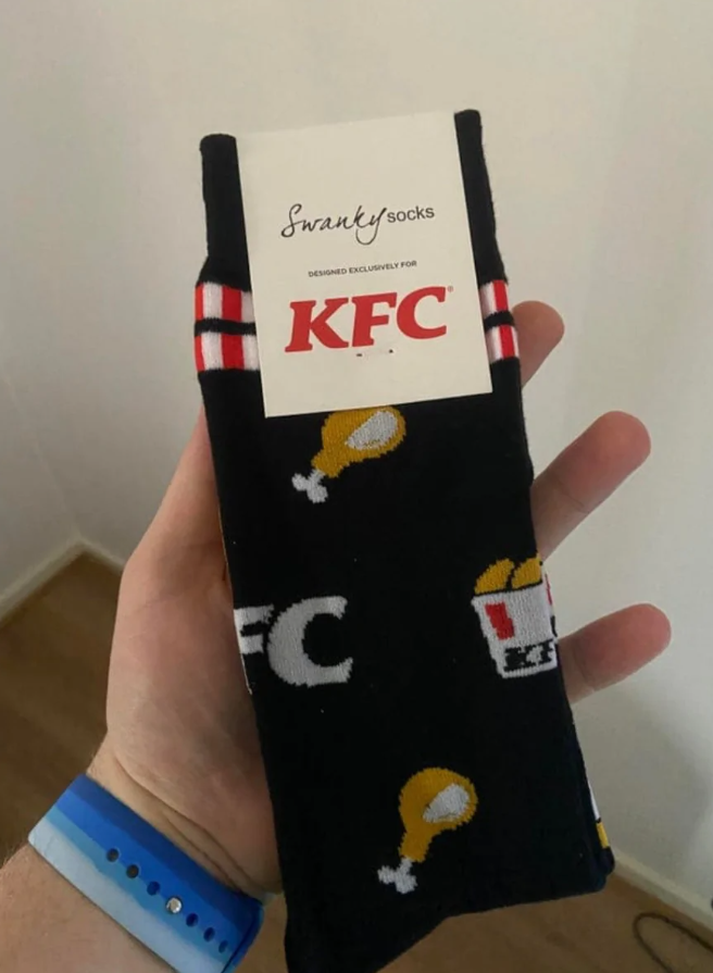 Čierne ponožky s motívom KFC v ruke, zdobené symbolmi kuraťa a logom KFC.