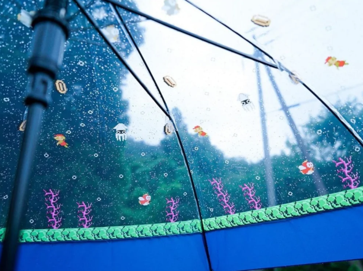 Priehľadný dáždnik s motívom pixelových postavičiek a morského sveta v dažďových kvapkách.
