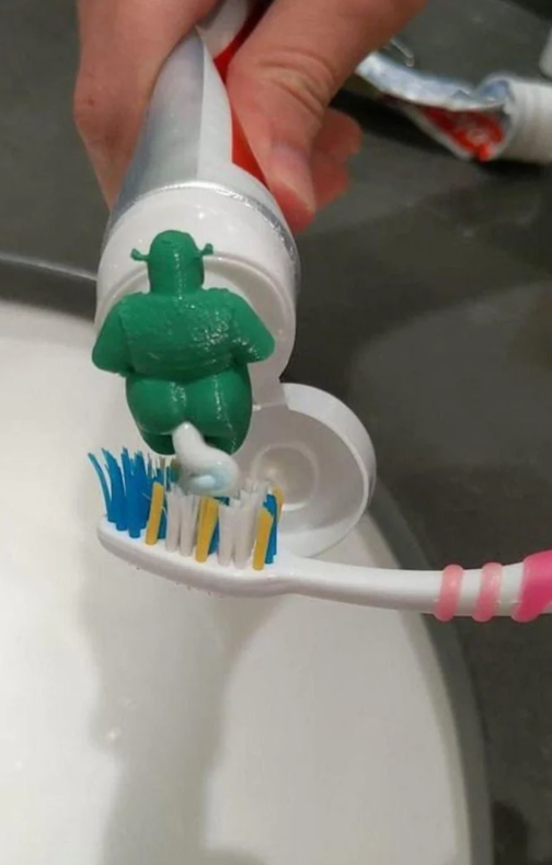 Zelená postavička vytláča pastu na farebnú zubnú kefku v kúpeľni.
