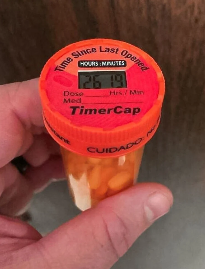 Fľaštička s tabletkami, oranžový časovač ukazuje 26 hodín od posledného otvorenia.