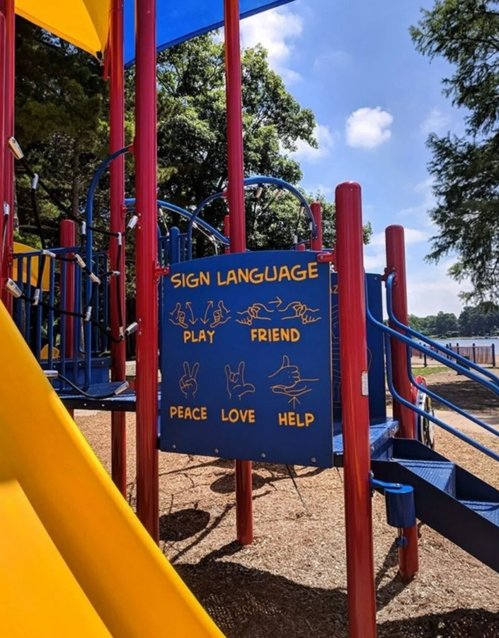 Detské ihrisko s tabuľou znakového jazyka zobrazujúcou slová: hrať, priateľ, mier, láska a pomoc.
