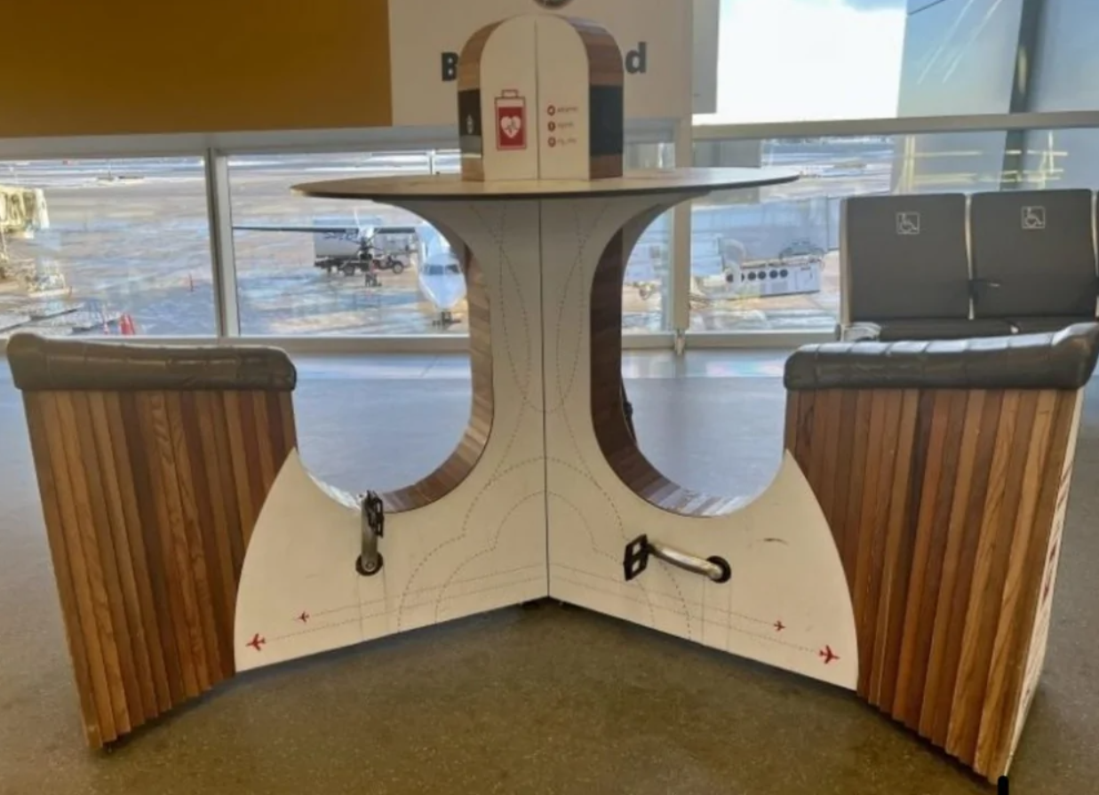 Moderná lavička s drevenými a bielymi prvkami na letisku, výhľad na lietadlá cez okno.