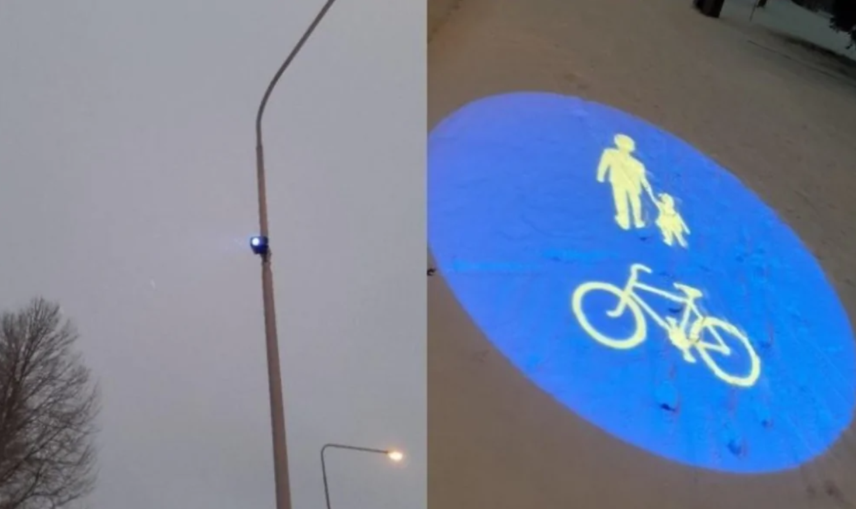 Pouličná lampa s premietaním grafiky pre chodcov a cyklistov na zasnežený chodník večer v meste.