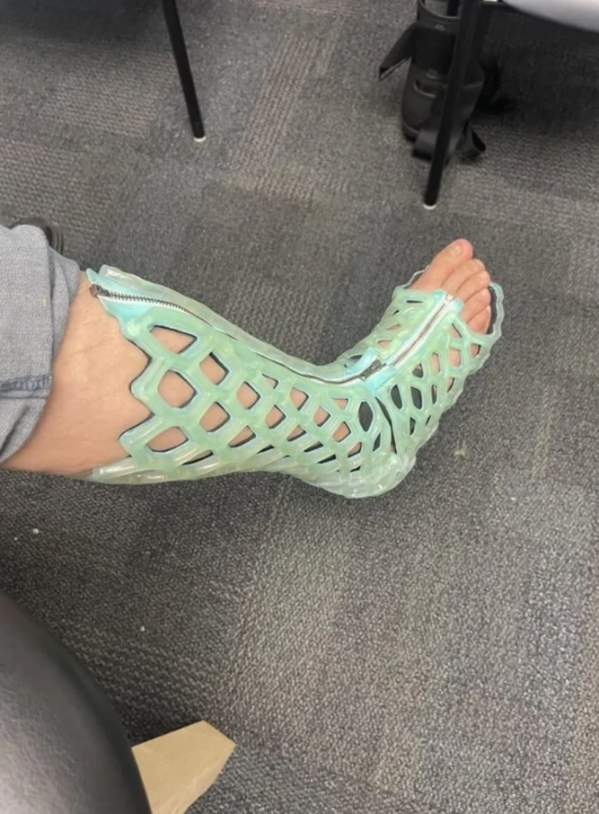 Osoba na sebe má priesvitné, sieťované sandále v mätovej farbe na šedom koberci.