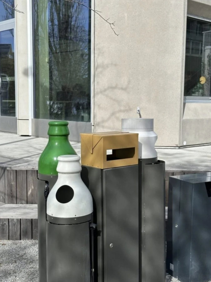 Odpadkové koše pred modernou budovou s recyklačnými otvormi v rôznych farbách.