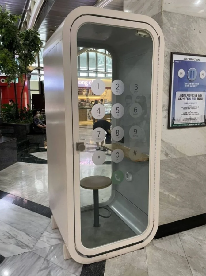 Verejná telefónna búdka v modernom nákupnom centre so stolom a stoličkou vo vnútri.