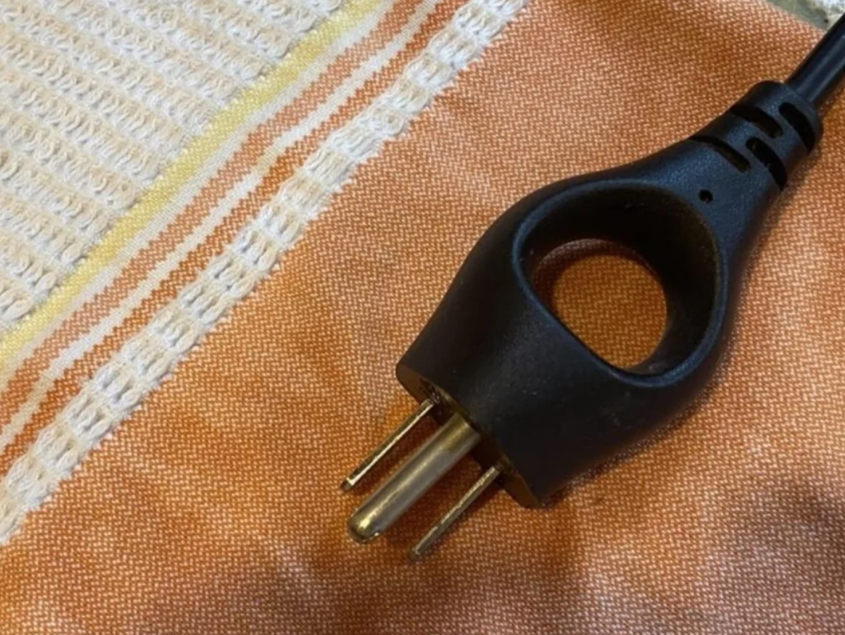 Čierny trojkolíkový zástrčkový kábel ležiaci na oranžovej a bielej tkanine.