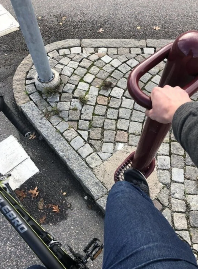 Osoba na bicykli sa opiera o stojan na nohu na bicyklovej ceste, dlažba na pozadí.