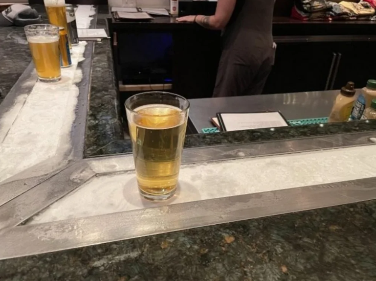 Pohár zlatej tekutiny na chladenej tyči v bare, pripravený na osvieženie a vychutnanie si atmosféry podniku.