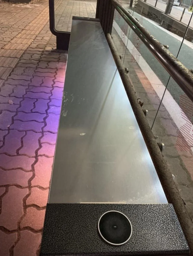 Plechová lavička na autobusovej zastávke, moderný dizajn s lampou a reproduktorom, udržiava čisté prostredie.