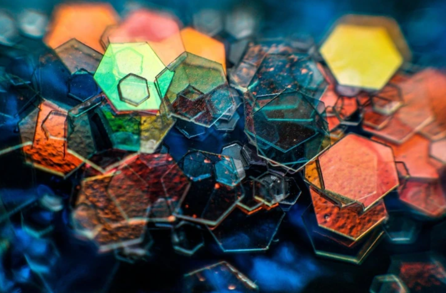 Farebné šesťuholníkové sklá vo vrstvách, vytvárajúce kaleidoskopický efekt na modrom pozadí.