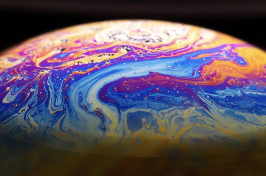 Pestrofarebná abstraktná štruktúra pripomínajúca povrch planéty v dúhových odtieňoch.