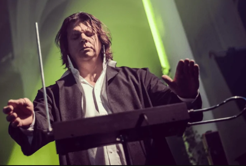 Hudobník hrá na theremin, zameranie na gestá rúk a elektronický nástroj, zelené osvetlenie pozadia.