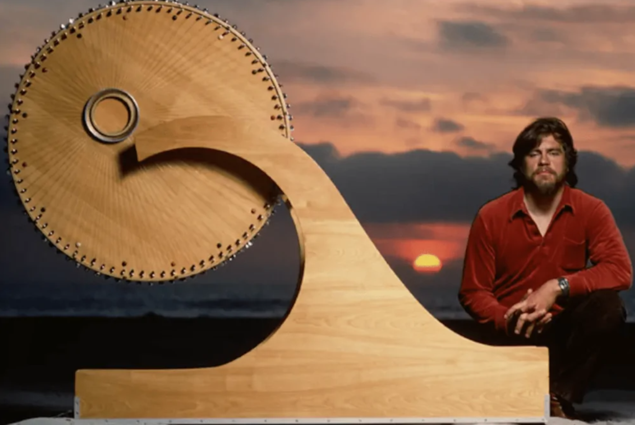 Človek sedí pri drevenej soše pred západom slnka na pláži, v pozadí obloha s farebnými mrakmi.