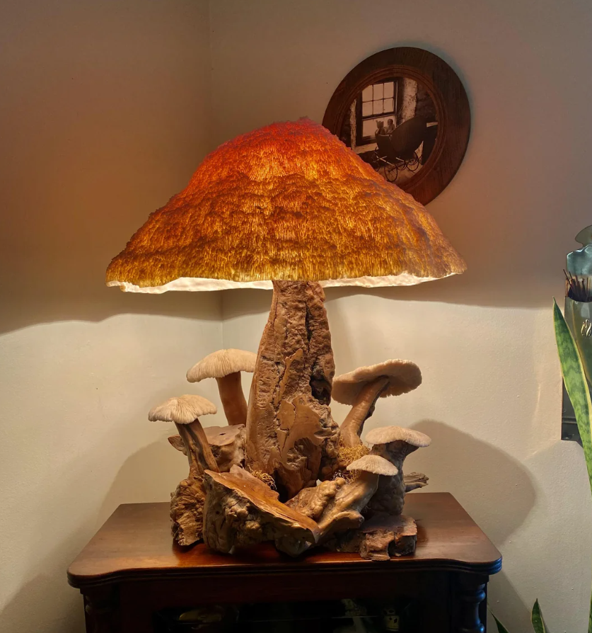 Lampa v tvare huby s rustikálnym dreveným podstavcom a žiarivým klobúkom na stole v útulnej miestnosti.