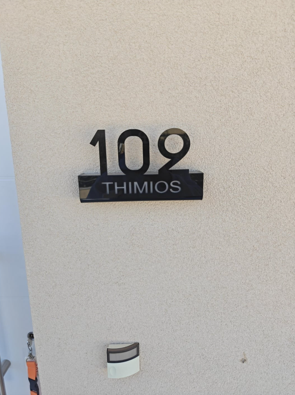 Číslo domu 109 s nápisom THIMIOS na bledom pozadí steny.