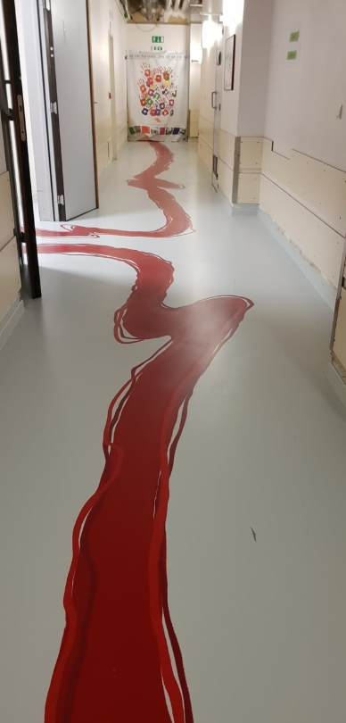 Červená grafika na podlahe chodby vedie k dverám s farebným motívom, osvetlený priestor s otvorenými dverami.