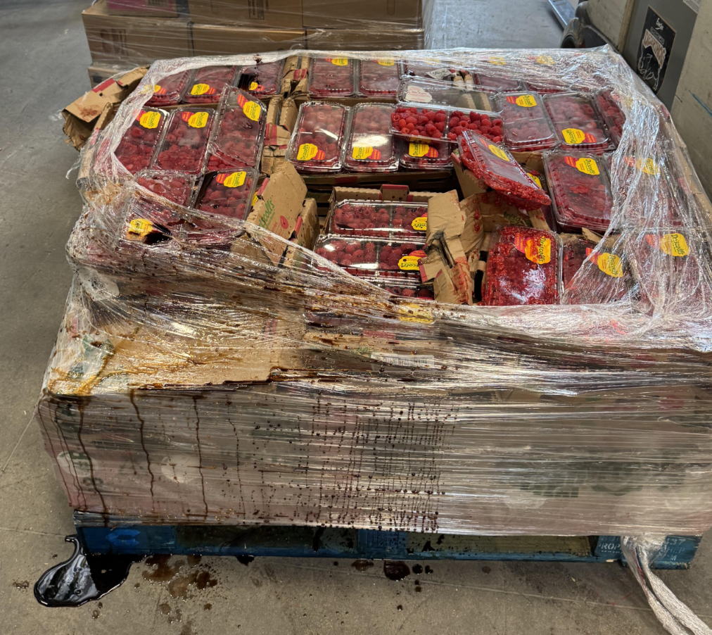 Zabalené jahody na palete s poškodením, pod ktorým uniká šťava na betónovej podlahe skladu.