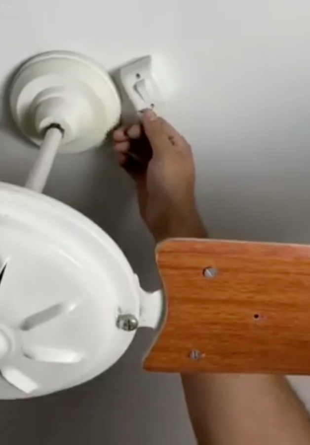 Ruka prepína elektrický vypínač vedľa stropného ventilátora s drevenými lopatkami.
