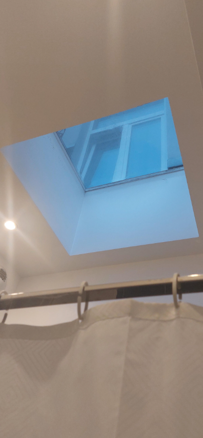 Okná v strope kúpeľne osvetľujú miestnosť modrým svetlom, sprchový záves je pripevnený na tyči.