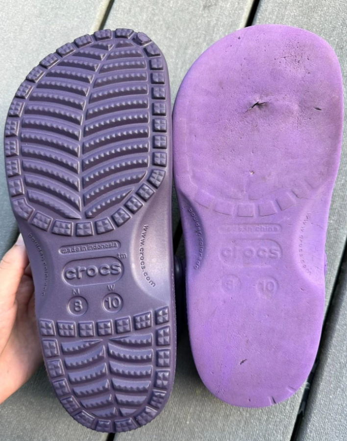 Podošvy fialových sandálov Crocs s rôznym vzorom a opotrebovaním na drevenej podlahe.