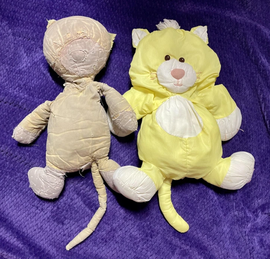 Dve staré plyšové hračky na fialovej prikrývke, jedna bledá, druhá žltá s bielymi prvkami.