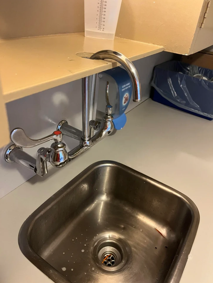 Vodovodná batéria s netradičnou inštaláciou v kuchynskom dreze, nesprávne umiestnená cez poličku.