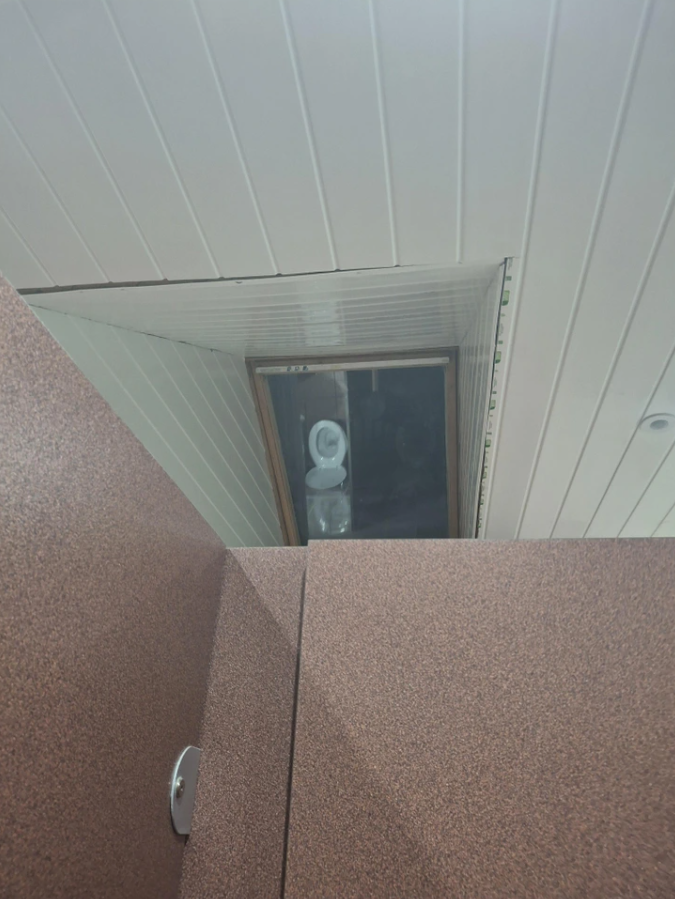 Stropný okno s ventiláciou nad kabínkou v interiéri, pohľad zospodu, biele a hnedé povrchy.