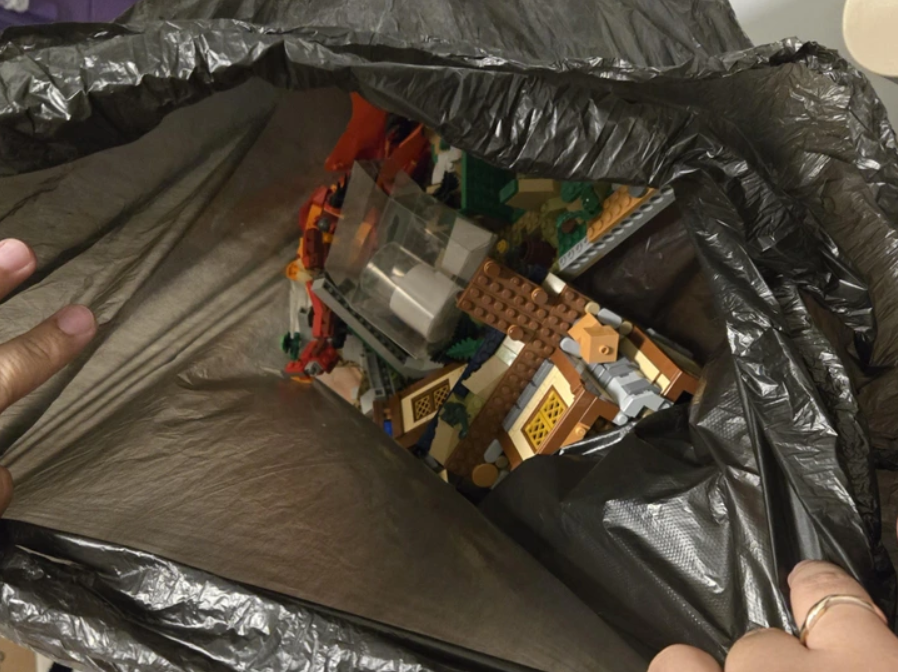 Čierny plastový sáčok plný rozložených Lego kociek rôznych farieb a tvarov.