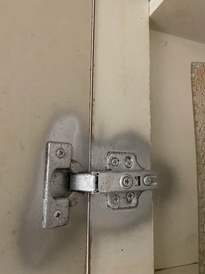 Kovový pánt na drevených dverách skrinky so stopami opotrebenia a hrdze.