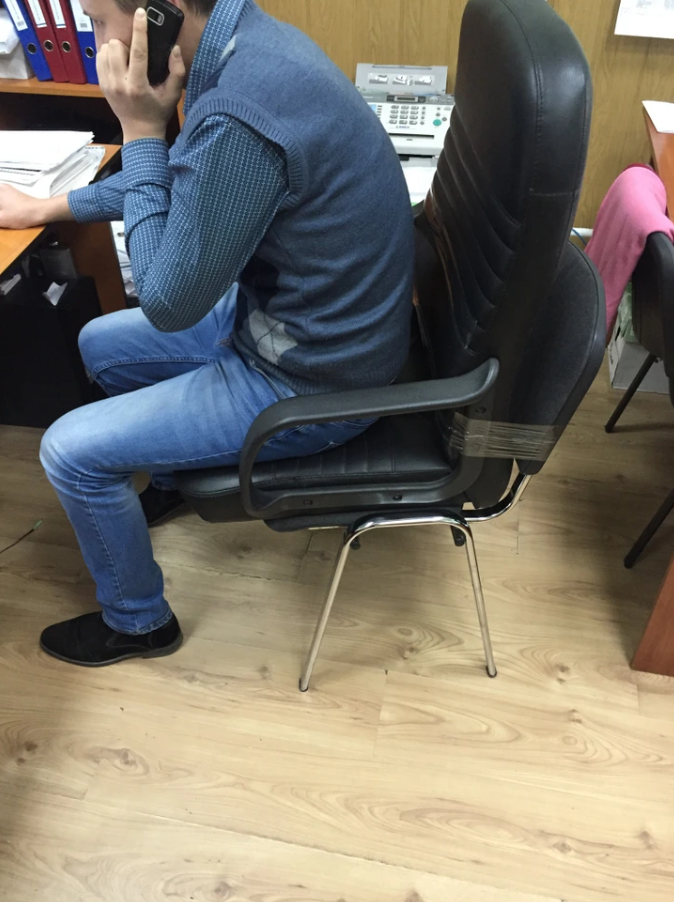 Osoba sediaca na stoličke s kartónom a viazacou páskou, telefonuje v kancelárii.