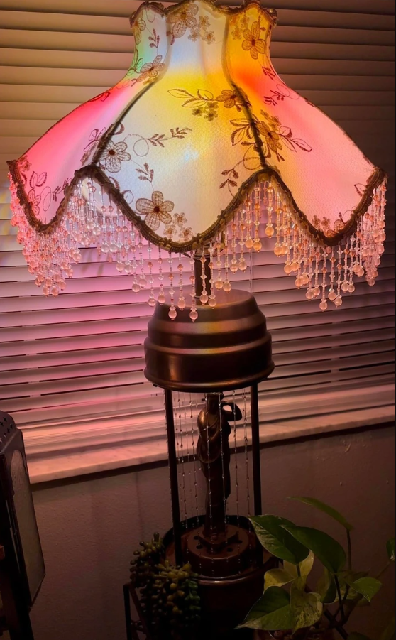 Retro lampa s kvetinovým tienidlom a korálkovým lemom, žiarivá svetelná dekorácia na parapete s rastlinou.