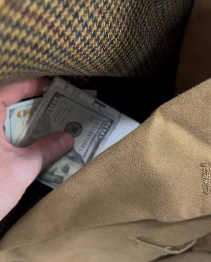 Ruka v kabáte s americkými dolármi, zrejme ukazujúca úschovu hotovosti alebo tajnú transakciu.