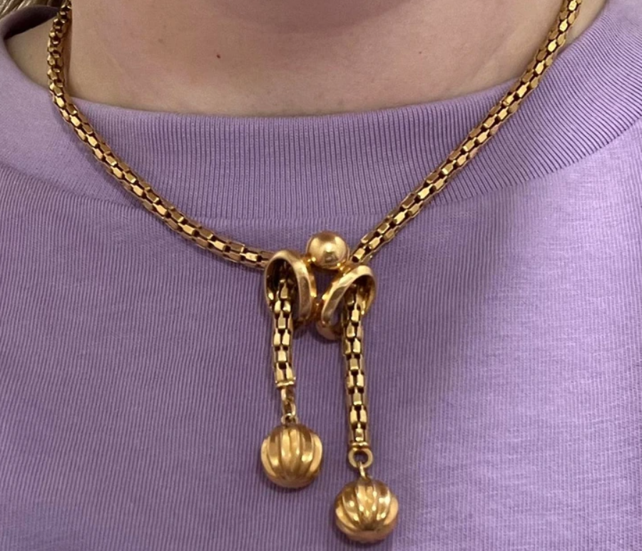 Zlatý náhrdelník s dekoratívnymi príveskami na fialovom svetri.
