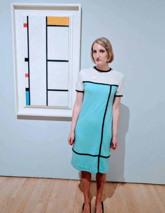 Žena v šatách inšpirovaná obrazom Pieta Mondriana v galérii, abstraktné umenie spája módu s modernizmom.