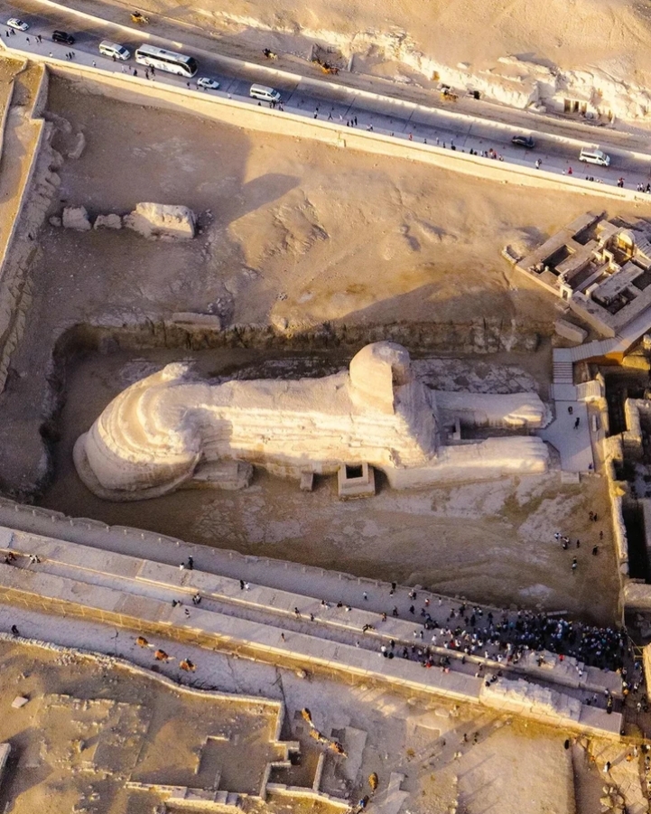 Letecký pohľad na Veľkú sfingu v Gíze obklopenú turistami a púšťou, s cestou a vozidlami v pozadí.